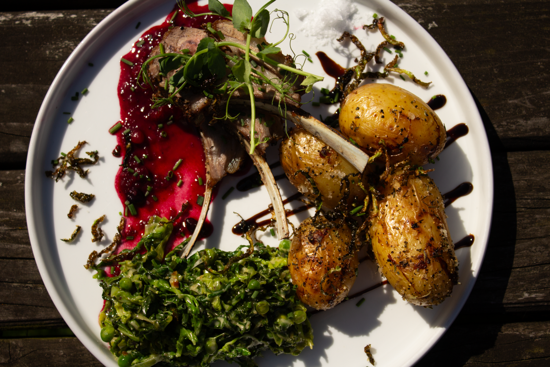 A gourmet dish with lamb chops, roasted potatoes, green vegetables, and a red sauce