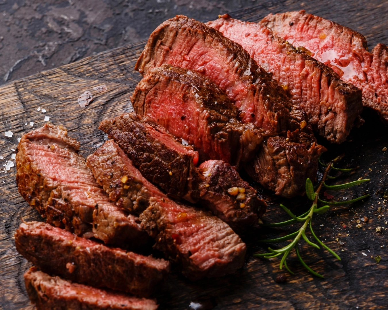 Medium-rare sliced steak on a wooden board with herbs and salt